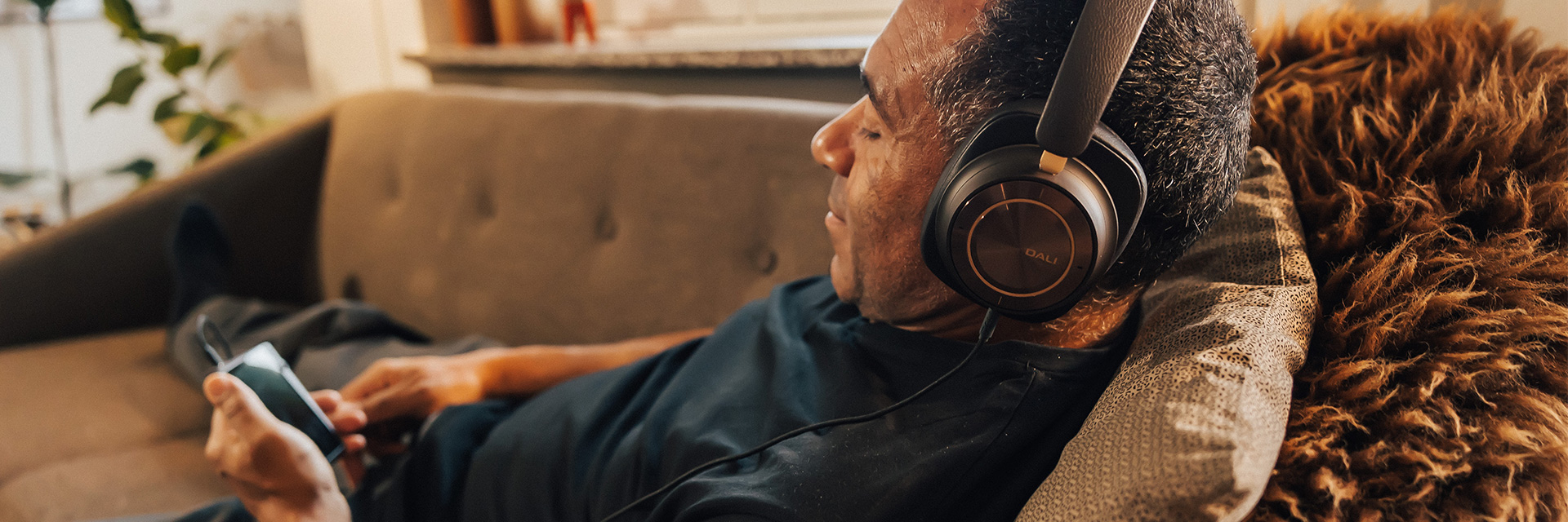 Man relaxing in couch with the DALI IO-12 headphones on.
